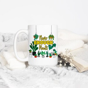 Puede incluir: Taza de cer&aacute;mica blanca con un gr&aacute;fico verde y amarillo de plantas y el texto "Never Enough Plants".