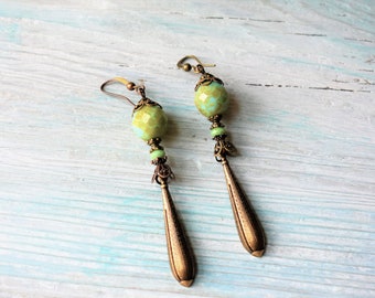 May include: A pair of long, green and bronze earrings with a large, round, green and white bead at the top of each earring.