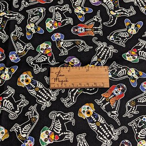 Puede incluir: Tela negra con un patrón repetido de perros esqueleto blancos con detalles de calavera de azúcar de colores. La tela tiene 7 pulgadas de ancho.