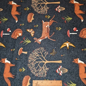 Pode incluir: Um tecido azul escuro com um padrão repetitivo de animais da floresta, árvores, cogumelos e borboletas. O padrão inclui veados, raposas, ouriços e pássaros. O tecido é medido com uma régua em centímetros.