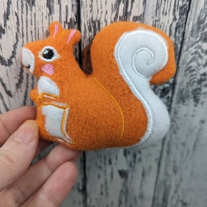 May include: A plush orange squirrel toy with a white fluffy tail. The squirrel has embroidered eyes and a pink nose.