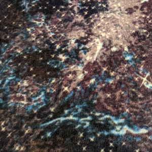 May include: A close-up of a dark blue, brown, and white fabric with a galaxy-like pattern. The fabric has a soft, fuzzy texture.
