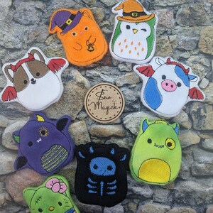May include: Nine felt Halloween-themed plush toys with embroidered details. The toys include a cat, owl, cow, bat, skeleton, and three monsters. The toys are all different colors and have different facial expressions.