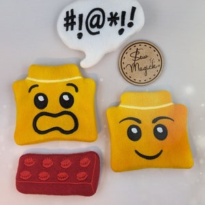 Puede incluir: Cuatro juguetes de peluche de fieltro con forma de ladrillos Lego. Dos son amarillos con caras bordadas, uno es rojo con puntos negros y uno es blanco con texto negro que dice "#!@*!". Un círculo marrón con el texto "Sew Magick" está en el fondo.