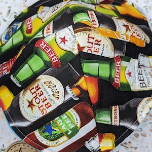 May include: A black kippah with a blue trim. The kippah is covered in a pattern of beer bottles with various labels, including "Strong Beer", "Lager Beer", and "Stout Beer".