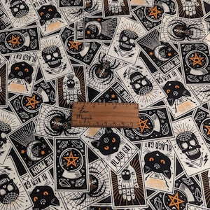 Puede incluir: Tela negra y blanca con un patrón repetido de cartas de tarot. Las cartas presentan imágenes de un gato negro, una calavera, una bola de cristal, una luna creciente y una mano con un ojo. Las cartas tienen una estética vintage y de ocultismo.