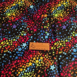 May include: Black fabric with a rainbow star pattern. The stars are of varying sizes and are scattered randomly across the fabric. The fabric is textured and has a slight sheen.