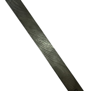May include: A rectangular, patterned metal blade with a wavy, layered design. The blade has a dark, mottled appearance, with shades of gray and black. The blade is angled diagonally across a white background.