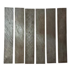 May include: Six rectangular metal blanks with unique, swirling patterns. The steel pieces vary in texture and design, showcasing a range of artistic finishes. The blades are arranged vertically, displaying their individual characteristics.