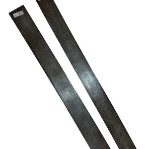 May include: Two long, rectangular, dark gray metal pieces with a textured surface. Each piece has a small white label with a number on it. The pieces are angled towards the viewer.
