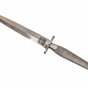 May include: A silver dagger with a double-edged blade and a textured handle. The dagger features a crossguard and a small emblem near the handle. The blade is pointed and the handle has a textured, non-slip grip.