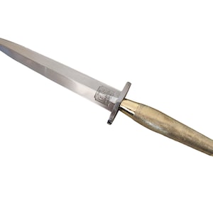 May include: A silver dagger with a double-edged blade and a gold-colored handle. The handle has a textured, diamond-patterned grip. The dagger features a crossguard and a rounded pommel. The blade is pointed and tapers to a sharp tip.
