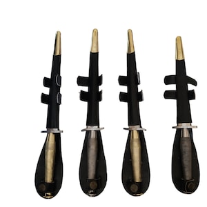 Può includere: Quattro oggetti in pelle nera e metallo con punte dorate e basi argentate. Ogni oggetto ha una forma cilindrica con un componente argentato a forma di proiettile visibile all'interno di un fodero in pelle nera. Gli oggetti sono disposti in fila su sfondo bianco.