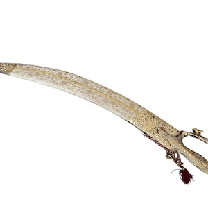 Puede incluir: Una espada curva ornamentada con empuñadura y vaina doradas. La hoja tiene un patrón floral. Una borla roja cuelga de la empuñadura. La espada está sobre un fondo blanco.