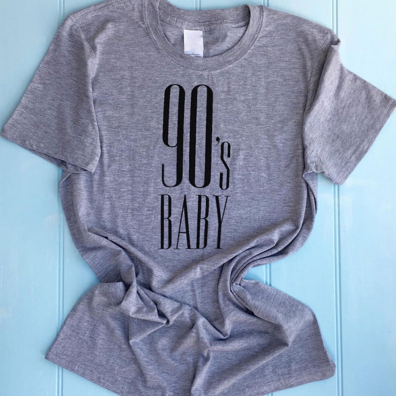 May include: A grey t-shirt with black text that reads "90's BABY".
