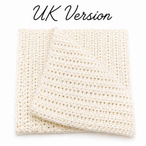 May include: Cream-colored, folded crochet blanket. The blanket is made of thick yarn, with a visible stitch pattern. The text "UK Version" is written in cursive at the top of the image.