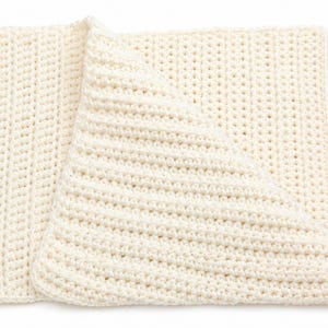 May include: Cream-colored, handmade crochet blanket. The blanket is folded, revealing a textured pattern of horizontal and vertical stitches. The soft, neutral color and simple design suggest a cozy, handcrafted item.