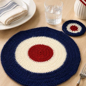 Può includere: Una tovaglietta rotonda all'uncinetto e un sottobicchiere più piccolo abbinato, entrambi caratterizzati da un motivo circolare concentrico in blu navy profondo, crema e rosso scuro. Gli articoli sono realizzati con un punto lavorato.