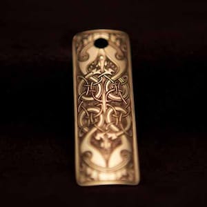 May include: A gold-colored metal bookmark with an intricate Celtic knot design. The bookmark has a hole at the top for hanging.