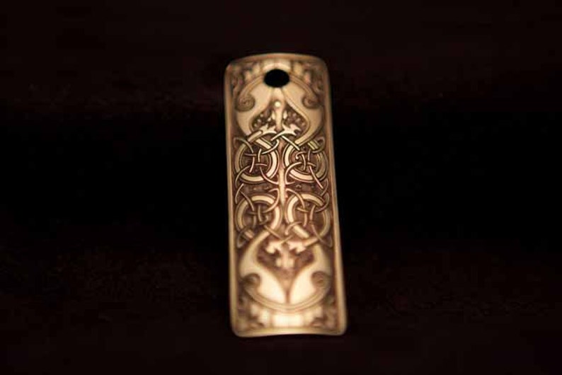 May include: A gold-colored metal bookmark with an intricate Celtic knot design. The bookmark has a hole at the top for hanging.