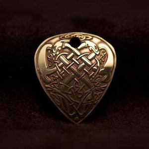 Könnte beinhalten: Ein goldfarbener Gitarren-Plektron aus Metall mit einem keltischen Knotendesign. Das Plektron ist herzförmig und hat oben ein Loch für eine Saite.