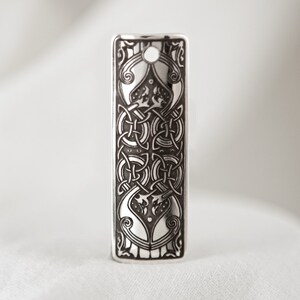 May include: A silver pendant with a detailed Celtic knot design. The pendant is rectangular and has a hole at the top for a chain.