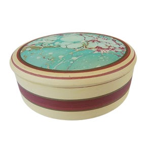 May include: Oval-shaped decorative box with a cream-colored base and a marbled turquoise and maroon lid. The box features maroon and cream-colored bands around the sides. The lid has a maroon border. A decorative storage container.