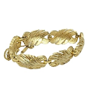 May include: A gold-toned bracelet featuring a textured feather design. The bracelet is composed of multiple feather-shaped links connected by small, circular links. The clasp is a simple hook and chain style.