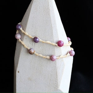 May include: A double-strand bracelet with pink and purple gemstone beads and a cream-colored cord.