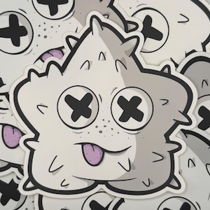 May include: A collection of stickers featuring a cartoon character with a white body, gray shading, and black cross-shaped eyes. The character has a purple tongue sticking out and small spikes around its head.