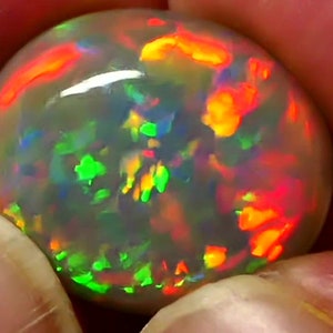 May include: A round, iridescent opal gemstone with a white base and flashes of green, orange, and red.
