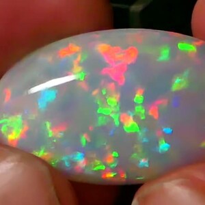 Puede incluir: Una piedra preciosa de ópalo blanco con un arcoíris de colores, incluyendo verde, rojo, naranja y azul.