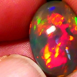 Könnte beinhalten: Nahaufnahme eines lebhaften, ovalen Opals. Der Opal zeigt ein faszinierendes Farbenspiel mit Schimmern in Rot, Orange, Grün und Blau.