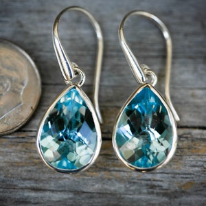 May include: A pair of silver drop earrings featuring teardrop-shaped blue topaz gemstones.