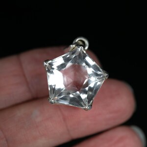 May include: A clear, faceted, star-shaped pendant set in a silver-toned metal frame. The pendant features multiple triangular facets that catch the light, creating a brilliant, reflective surface. It includes a small metal loop at the top for attachment.