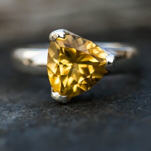 May include: A silver ring with a triangular, faceted, yellow gemstone.