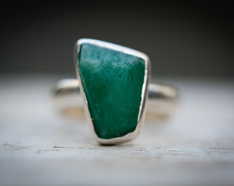 May include: A silver ring with a large, green, faceted gemstone set in the center.