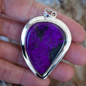 May include: A teardrop-shaped pendant with a purple and black stone set in a silver frame.