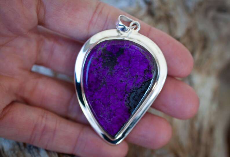 May include: A teardrop-shaped pendant with a purple and black stone set in a silver frame.