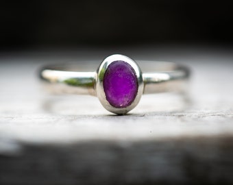 May include: A silver ring with a purple gemstone set in a bezel setting.