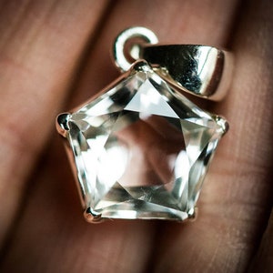 May include: A star-shaped clear gemstone pendant set in a polished silver-toned metal prong setting. The faceted stone features a five-pointed star silhouette with a smooth, reflective surface and a silver-toned bail attached to the top point.