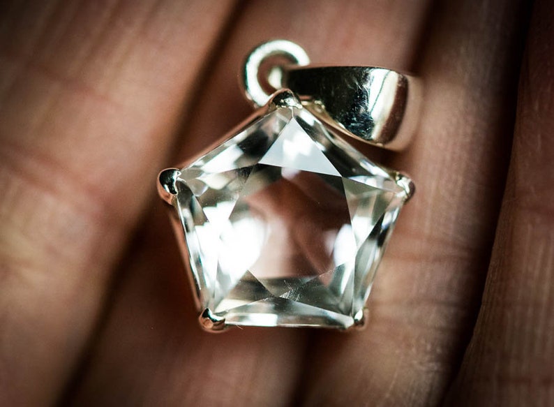 May include: A star-shaped clear gemstone pendant set in a polished silver-toned metal prong setting. The faceted stone features a five-pointed star silhouette with a smooth, reflective surface and a silver-toned bail attached to the top point.
