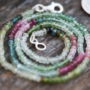 May include: A multi-strand necklace made of small, faceted gemstones in shades of pink, green, and blue. The necklace is made of natural gemstones and has a silver clasp.