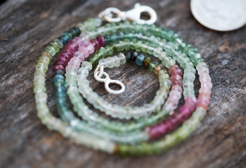 May include: A multi-strand necklace made of small, faceted gemstones in shades of pink, green, and blue. The necklace is made of natural gemstones and has a silver clasp.