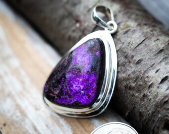 May include: A silver pendant with a purple and black gemstone. The pendant is shaped like a teardrop and has a silver bail.