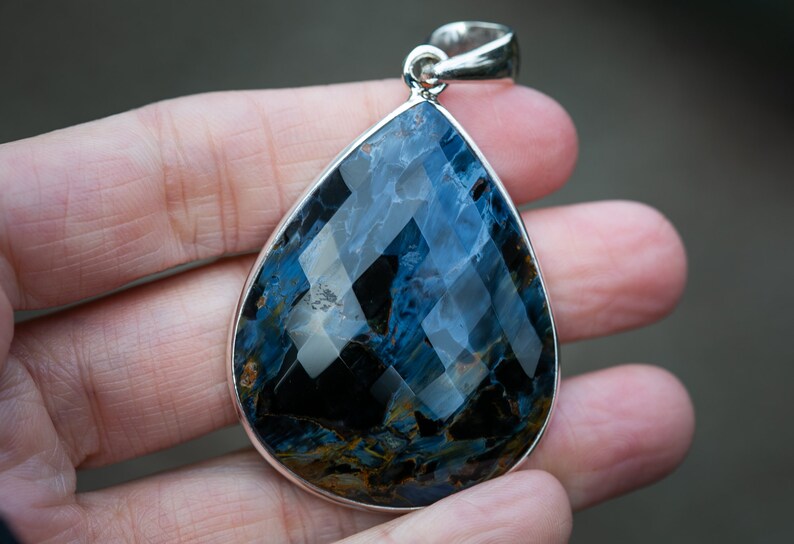 May include: A teardrop-shaped pendant with a blue and gold tiger's eye gemstone set in sterling silver.