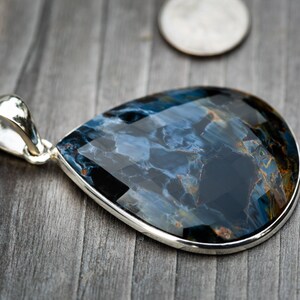 May include: A teardrop-shaped pendant with a blue and gold tiger's eye gemstone set in sterling silver.