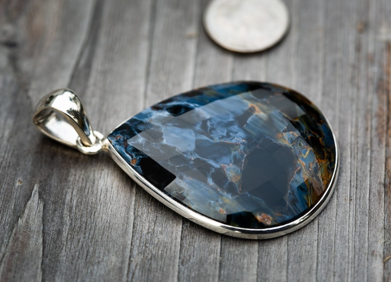 May include: A teardrop-shaped pendant with a blue and gold tiger's eye gemstone set in sterling silver.