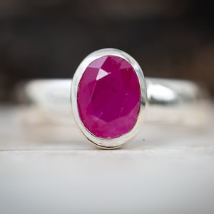 May include: A silver ring with a bright pink oval ruby gemstone.