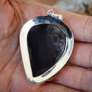 May include: A silver pendant with a dark grey stone set in a heart-shaped frame.